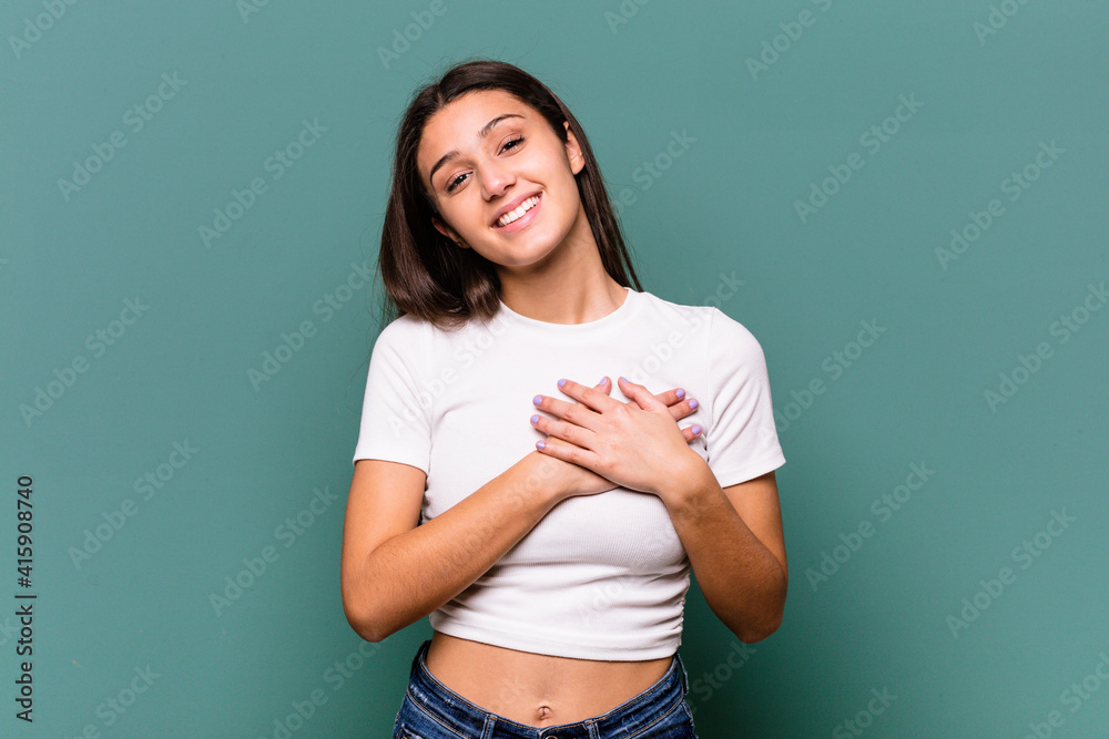 Young Indian woman isolated on blue background has friendly expression, pressing palm to chest. Love concept.