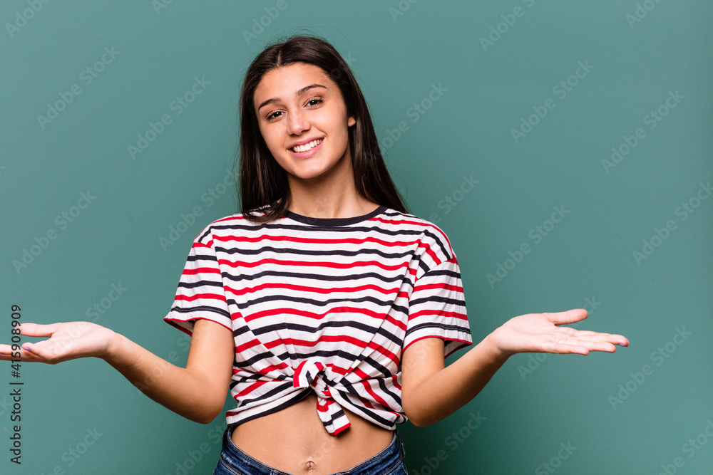 Young Indian woman isolated on blue background makes scale with arms, feels happy and confident.