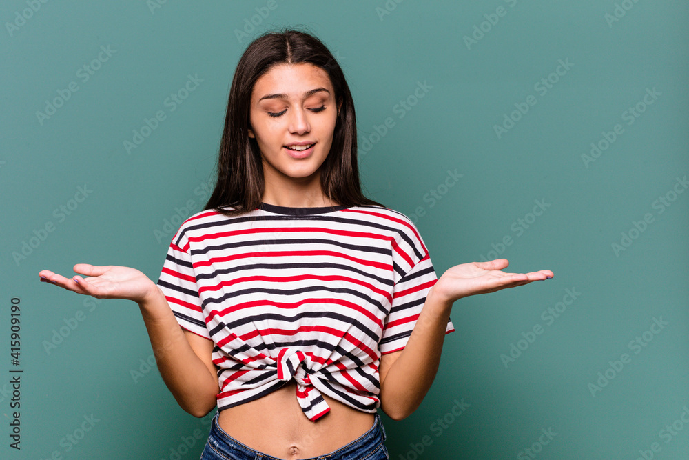 Young Indian woman isolated on blue background holding something with palms, offering to camera. Young Indian woman isolated on blue background holding something with palms, offering to camera.