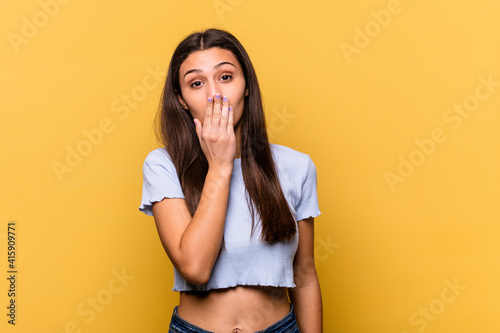 Young Indian woman isolated on yellow background shocked, covering mouth with hands, anxious to discover something new.