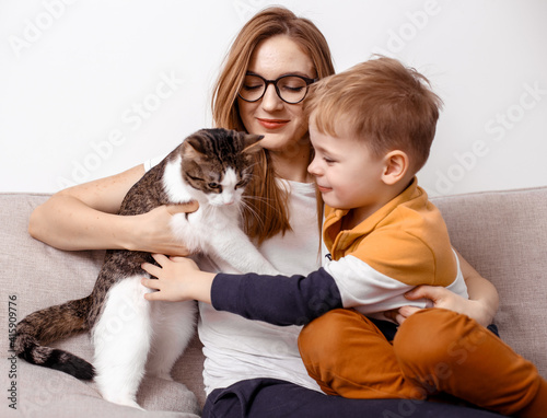Mommy, son and cat sits on the couch in the home interior. Concept inferior family, no father, modern woman. A happy family, mother, son and cat are sitting on the sofa feeling happy. Pet.