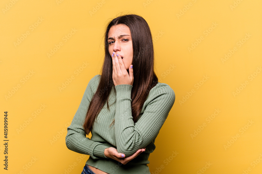Young Indian woman isolated on yellow background yawning showing a tired gesture covering mouth with hand. Young Indian woman isolated on yellow background yawning showing a tired gesture covering mouth with hand.