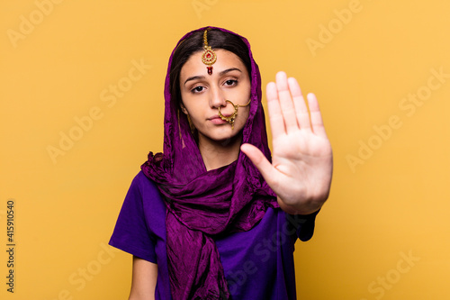 Young Indian woman wearing a traditional sari clothes isolated on yellow background standing with outstretched hand showing stop sign, preventing you.