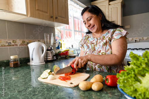 Happy Hispanic Mom Cooking Healthy Food - Mature Woman Cutting Fresh Vegetables In Her Kitchen - Woman Making Healthy Salad