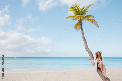 Happy Bikini woman sitting on palm tree at the caribbean ocean 