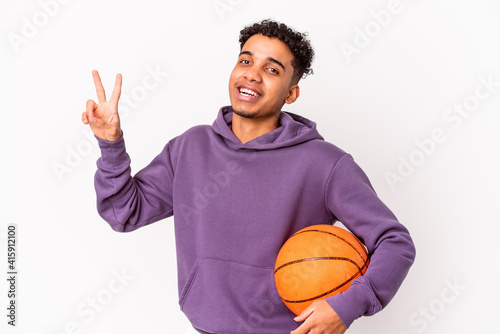 Young african american curly man isolated playing basketball joyful and carefree showing a peace symbol with fingers. © Asier