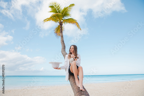 Woman rests at the palm tree near ocean at sunset