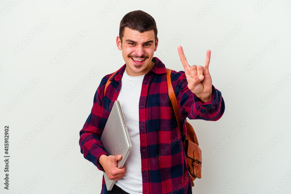 Young caucasian student man holding a laptop isolated on white background showing a horns gesture as a revolution concept. Young caucasian student man holding a laptop isolated on white background showing a horns gesture as a revolution concept.