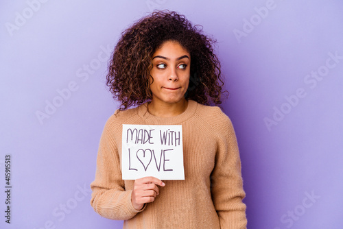 Young African American woman holding a Made with love placard isolated on purple background confused, feels doubtful and unsure.