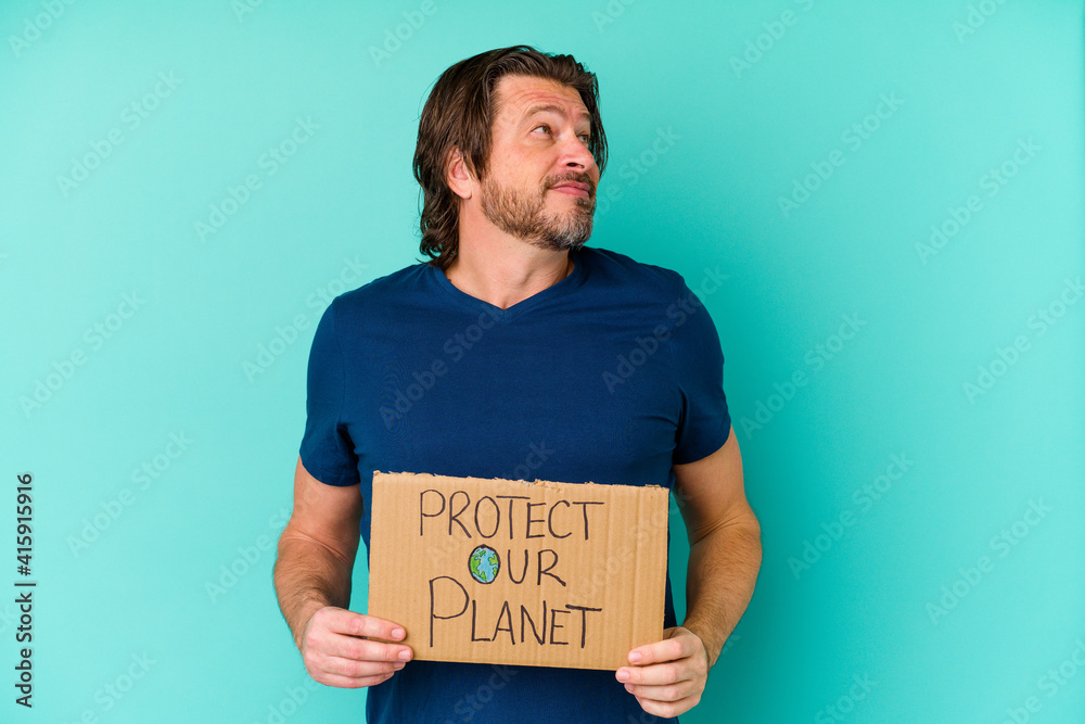 Middle age dutch man holding a protect our planet placard isolated on blue background dreaming of achieving goals and purposes Middle age dutch man holding a protect our planet placard isolated on blue background dreaming of achieving goals and purposes