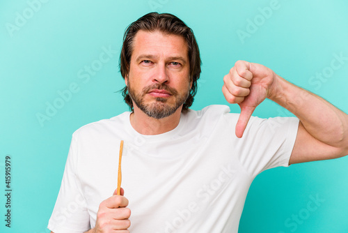 Middle age dutch man holding a toothbrush isolated on blue background showing a dislike gesture, thumbs down. Disagreement concept.