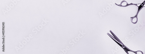 Banner flat lay from above of professional silver hair cutting shears set on purple background. Hairdresser salon equipment and haircut work tools concept during quarantine with copy space