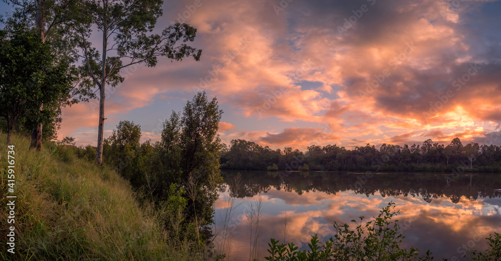 Fototapeta premium Panoramic Riverside Sunrise with Dramatic Cloud Reflections