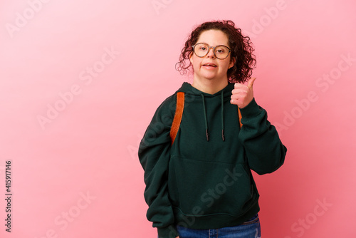 Young student woman with Down syndrome isolated on pink background smiling and raising thumb up © Asier