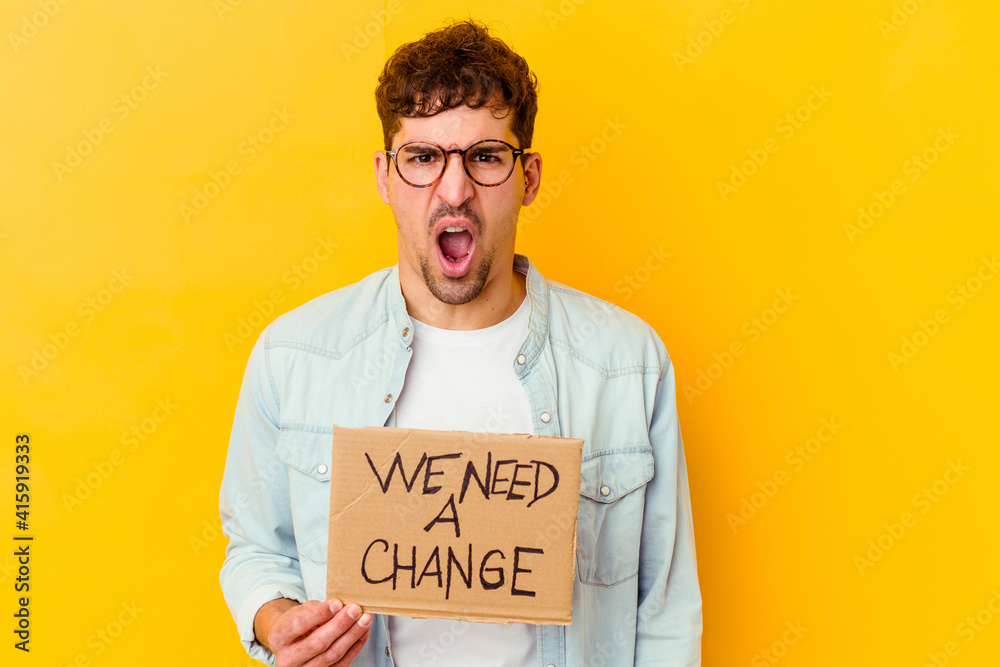 Young caucasian man holding a we need a change placard isolated screaming very angry and aggressive. Young caucasian man holding a we need a change placard isolated screaming very angry and aggressive.