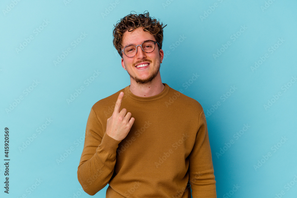 Young caucasian man wearing eyeglasses isolated on blue background pointing with finger at you as if inviting come closer. Young caucasian man wearing eyeglasses isolated on blue background pointing with finger at you as if inviting come closer.