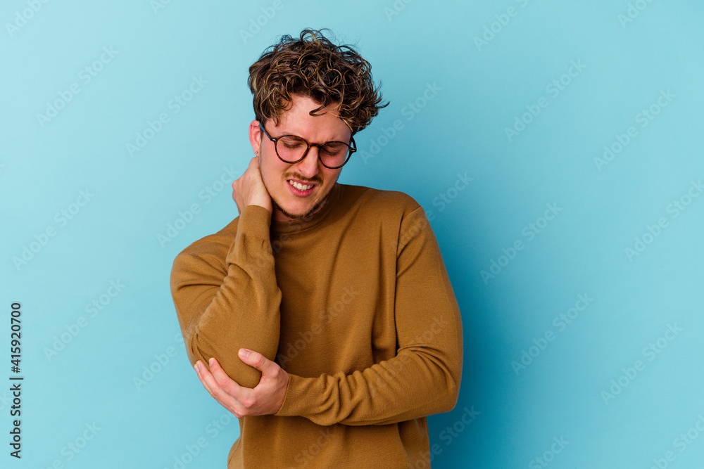 Young caucasian man wearing eyeglasses isolated on blue background massaging elbow, suffering after a bad movement.