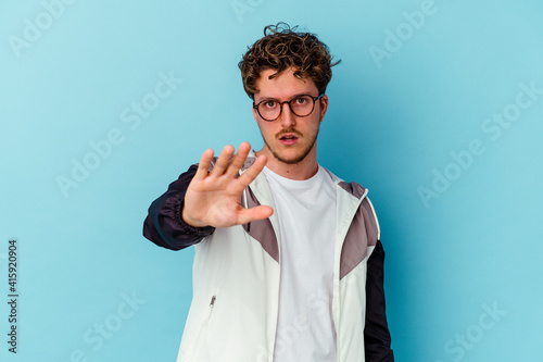 Young caucasian man wearing eyeglasses isolated on blue background being shocked due to an imminent danger