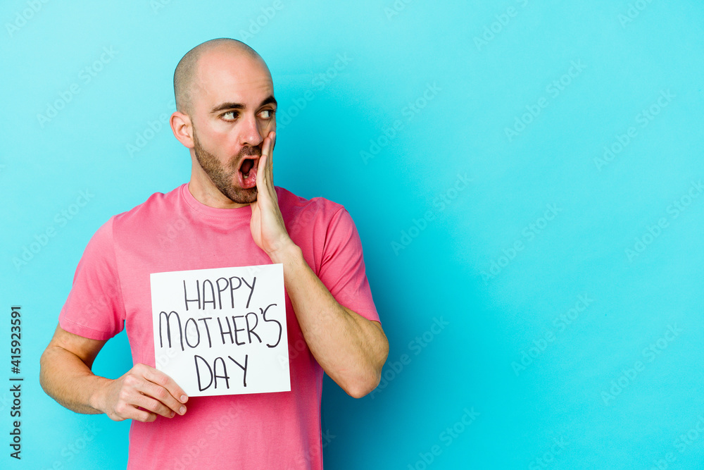 Young caucasian bald man holding a happy mothers day placard isolated on blue background is saying a secret hot braking news and looking aside Young caucasian bald man holding a happy mothers day placard isolated on blue background is saying a secret hot braking news and looking aside