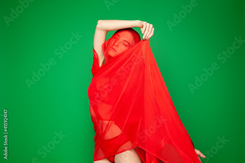 Dreamy woman under red veil against green background