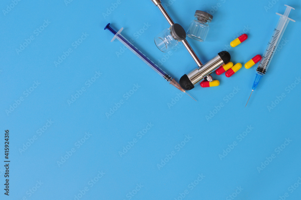 Layout of reflex hammer, syringes, glass vials and pills with blank space for text on blue background Layout of reflex hammer, syringes, glass vials and pills with blank space for text on blue background