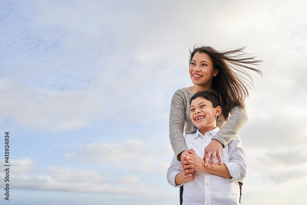 Young mother hugging her child against a bright blue sky with clouds. Latin people. Copy space. Young mother hugging her child against a bright blue sky with clouds. Latin people. Copy space.