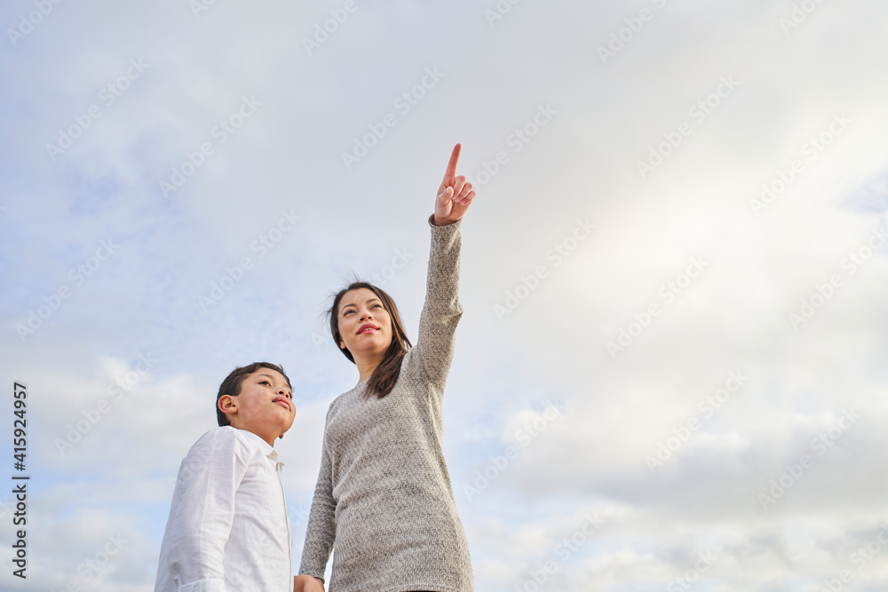 Young Latina mother with child pointing to some point against a bright blue sky with clouds. Family concept. Young Latina mother with child pointing to some point against a bright blue sky with clouds. Family concept.