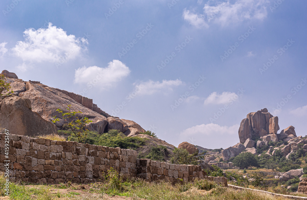 Chitradurga, Karnataka, India - November 10, 2013: Fort or Elusuttina Kote. Brown rocks and stone ramparts and war under blue cloudscape. Some green foliage. Chitradurga, Karnataka, India - November 10, 2013: Fort or Elusuttina Kote. Brown rocks and stone ramparts and war under blue cloudscape. Some green foliage.