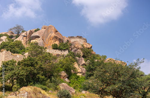 Chitradurga, Karnataka, India - November 10, 2013: Fort or Elusuttina Kote. Half circle rampart on top of boulder rock hill with more walls lower, green foliage under blue cloudscape. photo