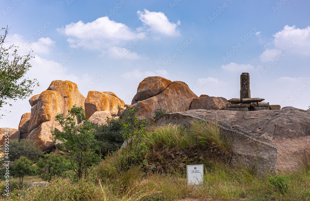 Chitradurga, Karnataka, India - November 10, 2013: Fort or Elusuttina Kote. Shivalingam gray stone pillar on rock plateau under blue cloudscape, green foliage and brown boulders.