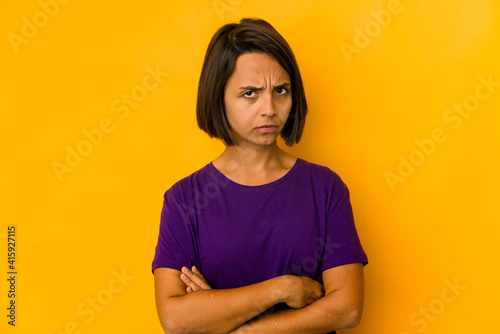 Young hispanic woman isolated on yellow frowning face in displeasure, keeps arms folded.