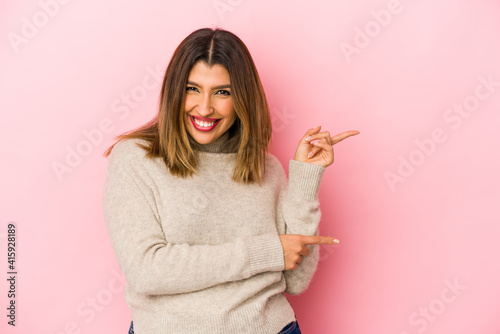 Young indian woman isolated on pink background excited pointing with forefingers away.