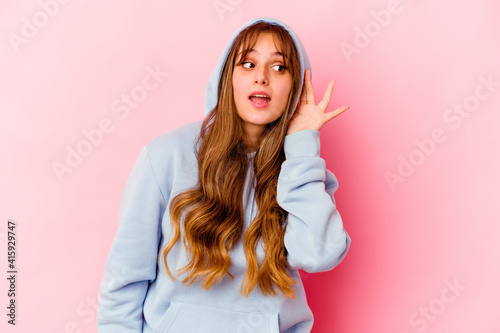 Young caucasian woman with hood isolated on yellow background trying to listening a gossip.
