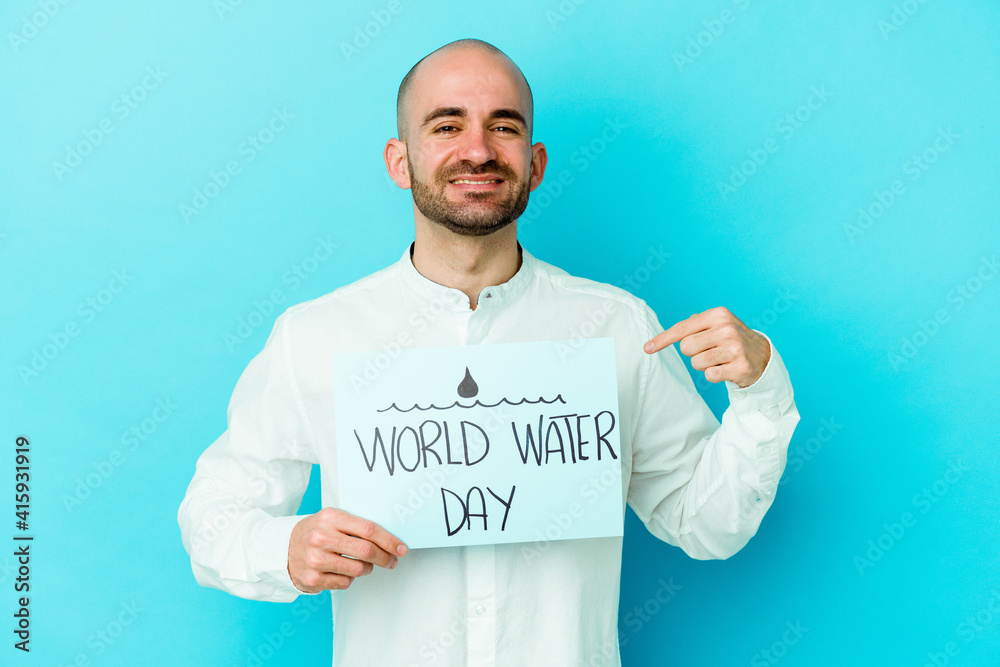 Young caucasian bald man celebrating world water day isolated on blue background person pointing by hand to a shirt copy space, proud and confident Young caucasian bald man celebrating world water day isolated on blue background person pointing by hand to a shirt copy space, proud and confident