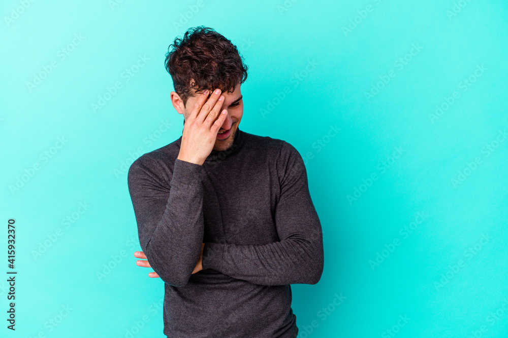 Young caucasian man isolated on blue background blink at the camera through fingers, embarrassed covering face. Young caucasian man isolated on blue background blink at the camera through fingers, embarrassed covering face.