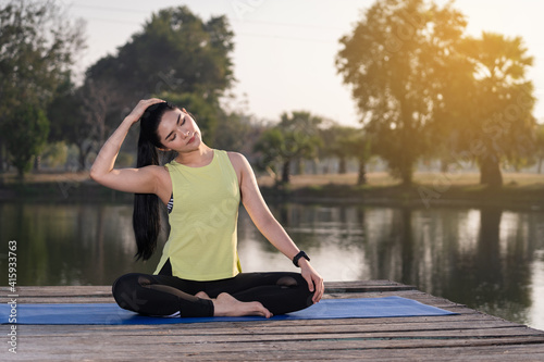 Young beautiful Asian woman in sports outfits doing yoga outdoor in the park in the morning with warm sunlight for a healthy lifestyle. Young woman yogi doing yoga in morning park © EduLife Photos