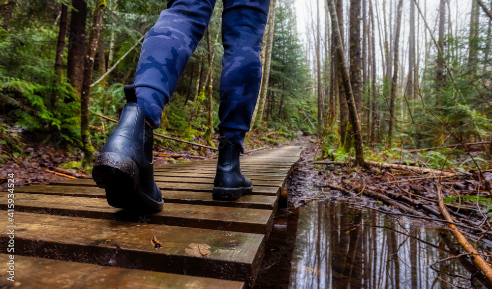 Girl Walking on a Mystical Trail in Rain Forest during a foggy and rainy Winter Season. Woods in Squamish, North of Vancouver, British Columbia, Canada. Low Angle Panorama