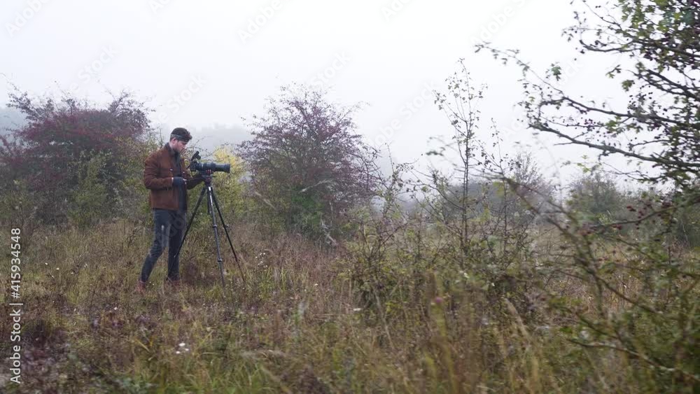 Photographer with a camera on a tripod,from behind a bush,misty. Photographer with a camera on a tripod,from behind a bush,misty.