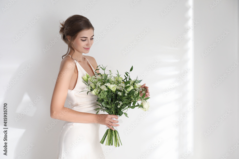 Young bride wearing wedding dress with beautiful bouquet on light background Young bride wearing wedding dress with beautiful bouquet on light background