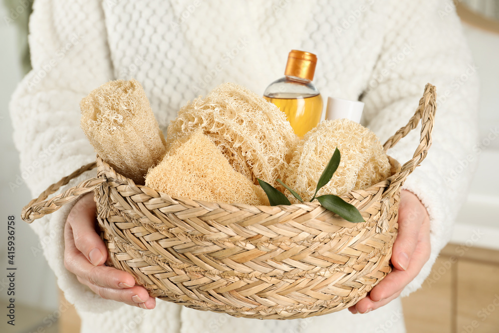 Woman holding wicker basket with natural loofah sponges in bathroom, closeup