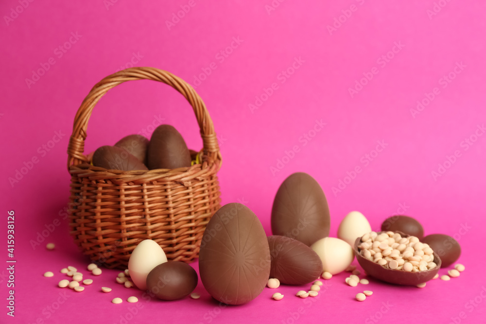 Sweet chocolate eggs and wicker basket on pink background Sweet chocolate eggs and wicker basket on pink background