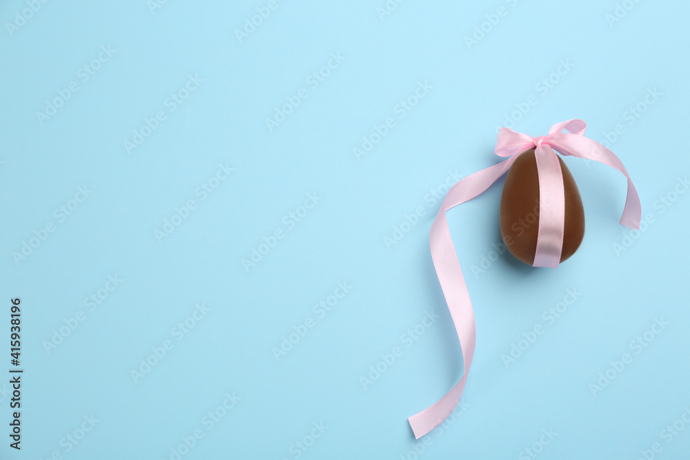 Sweet chocolate egg with pink bow on light blue background, top view. Space for text Sweet chocolate egg with pink bow on light blue background, top view. Space for text