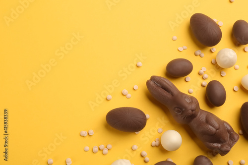 Flat lay composition with chocolate Easter bunny, eggs and candies on yellow background. Space for text