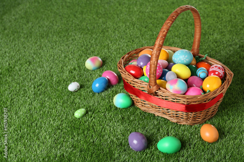 Wicker basket with Easter eggs on green grass. Space for text