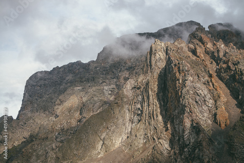 Scenic mountain landscape with great rocks in cloudy sky in vintage colors. Awesome sunny scenery with low clouds on rocky mountain top in pastel tones. Beautiful brown rock in sunlight and low clouds