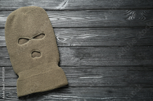 Beige knitted balaclava on black wooden table, top view. Space for text