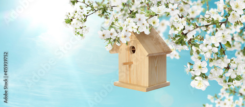 Beautiful wooden bird house hanging on blossoming tree outdoors, banner design. Springtime