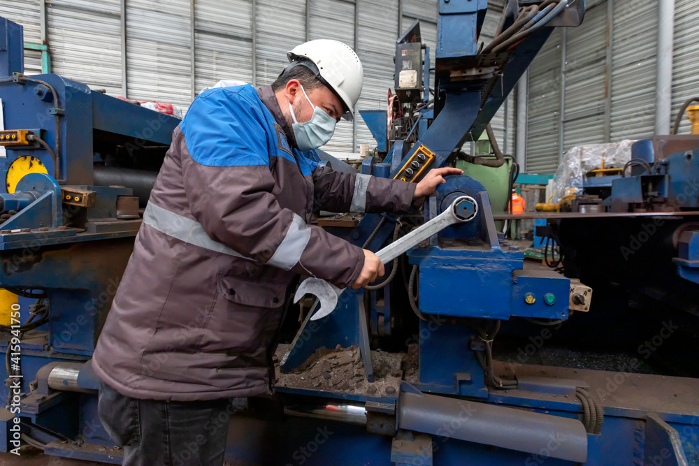 Worker is repairing to machine with screw wrench. A wrench or spanner is a tool used to provide grip and mechanical advantage in applying torque to turn objects usually rotary fasteners, such as nuts.