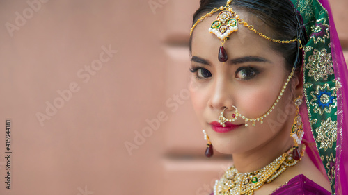 Portrait Asian woman in a margenta Indian tradition sari, she is looking at a camera next to the an orange wall photo