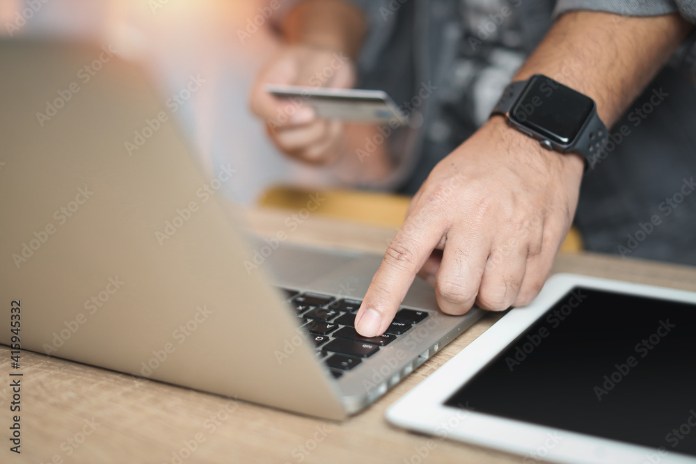 Man hands in casual jacket sitting and holding credit card and using laptop computer on table for online payment or shopping online. Business man using mobile phone while sitting. E-Banking concept Man hands in casual jacket sitting and holding credit card and using laptop computer on table for online payment or shopping online. Business man using mobile phone while sitting. E-Banking concept